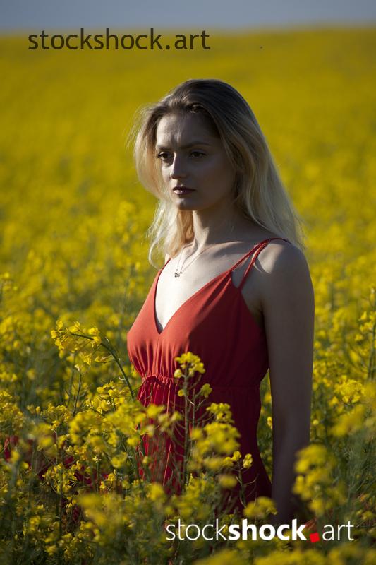 Girl in a red dress in yellow rapeseed, portrait, stock image