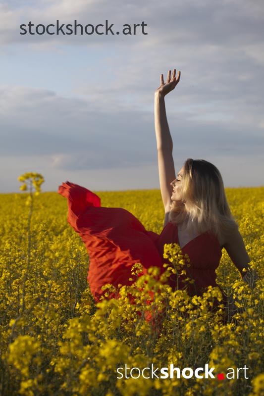 Girl in a red dress in yellow rapeseed, portrait, stock image