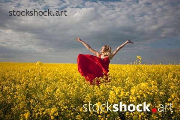 Girl in a red dress in yellow rapeseed, portrait, stock image
