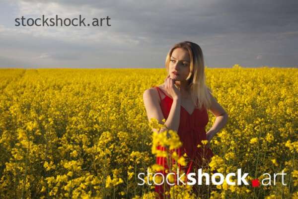 Girl in a red dress in yellow rapeseed, portrait, stock image