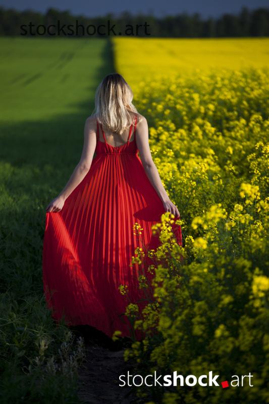 Girl in a red dress in yellow rapeseed and green grass