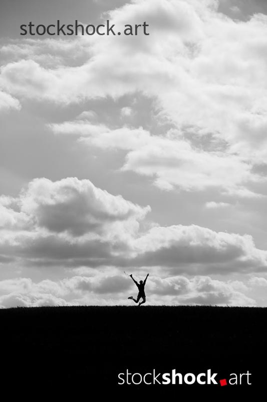 Happy person with open arms jumping against the background of clouds, b&w, stock image