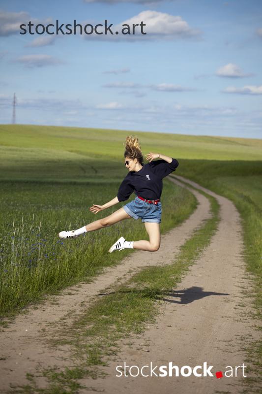 Young woman jumps over a dirt road