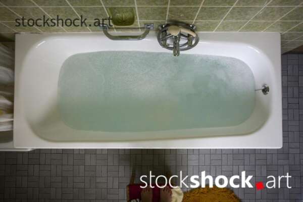 An old bathtub filled with water in a green bathroom - stock image