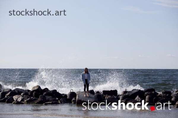 Girl on the rocks on the seashore against the background of the wave