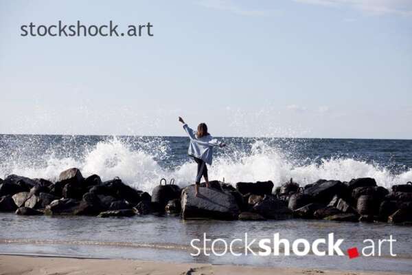 Girl on the rocks on the seashore against the background of the wave