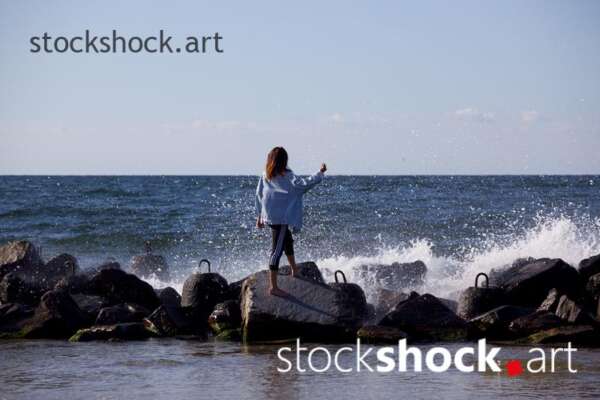Girl on the rocks on the seashore against the background of the wave