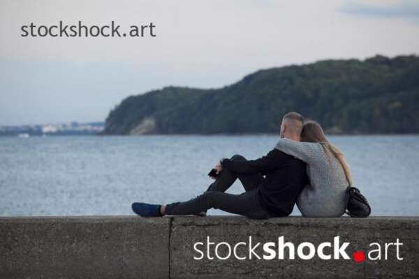 A couple sitting on a wall looking at the sea
