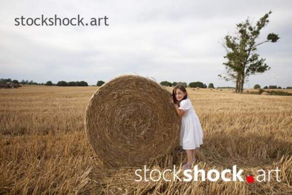 End of harvest, Girl pushing a bale of straw in a field during harvest, stock image, jowita niemczyk, stockshock.art