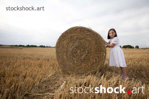 End of harvest, Girl pushing a bale of straw in a field during harvest, stock image, jowita niemczyk, stockshock.art