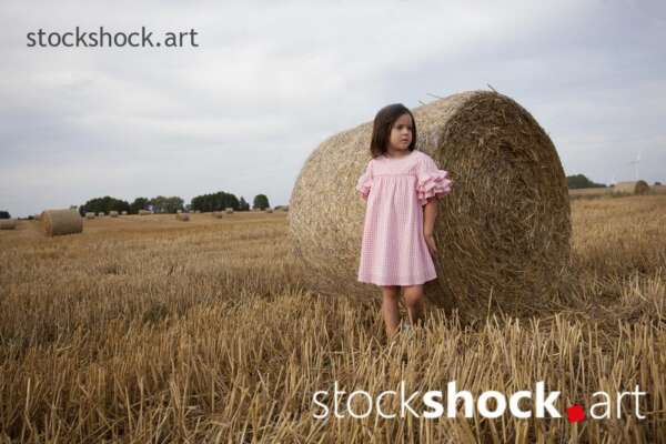 End of harvest, Girl standing by a bale of straw in a field during harvest, stock image, jowita niemczyk, stockshock.art