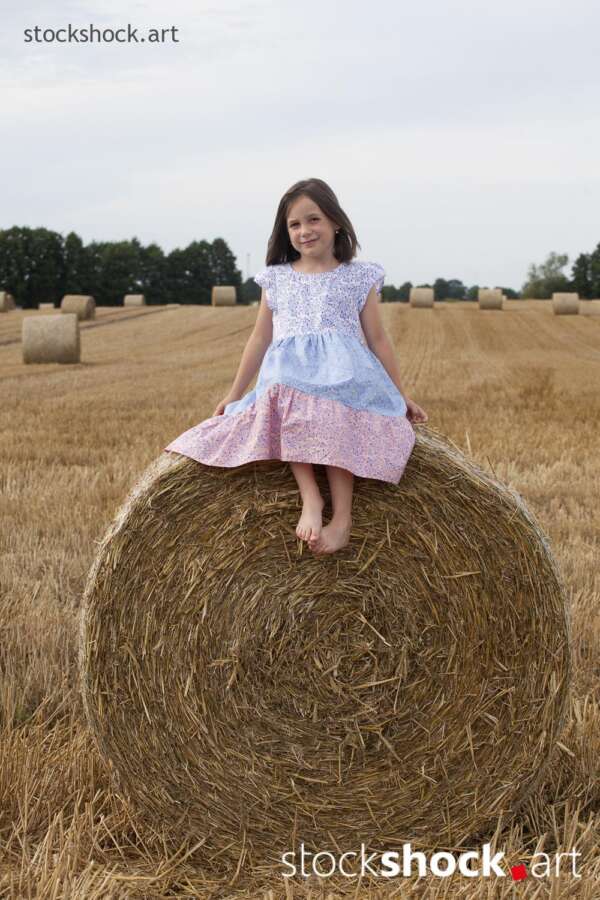 End of harvest, Girl sitting on a bale of straw in a field during harvest, stock image, jowita niemczyk, stockshock.art