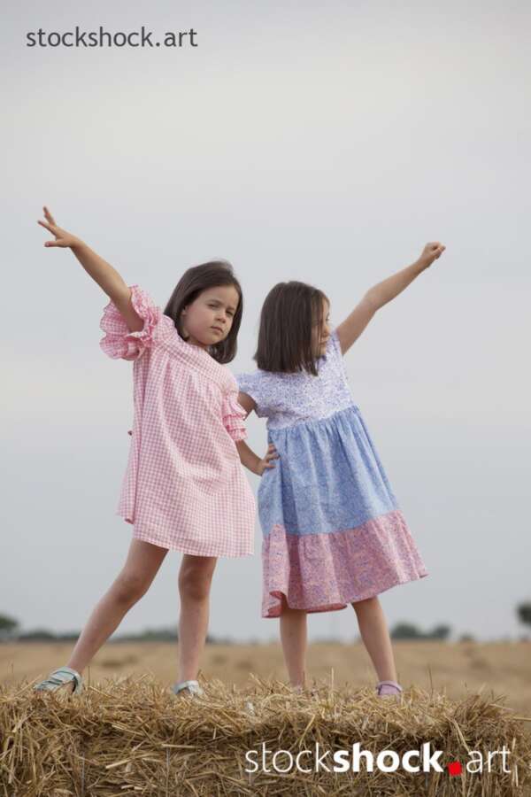 Two happy sisters play on bales during the summer harvest - stock image