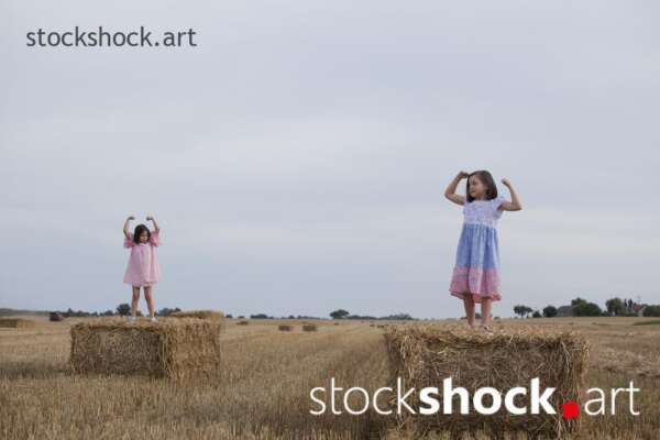Two happy sisters play on bales during the summer harvest - stock image