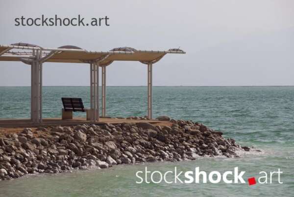Pier on the shore of the Dead Sea - stock image 3401 x 5102 pix jpeg | 54 x 35,99 cm | 300 dpi Canon 5d mk II A serene view of the Dead Sea with turquoise water and a pier on a sunny day. The Dead Sea, known for its high salt content and therapeutic properties, offers the perfect setting for relaxation. Sunny beach, turquoise water, Dead Sea, pier, relaxing on a chair, seaside tranquility, natural spa.