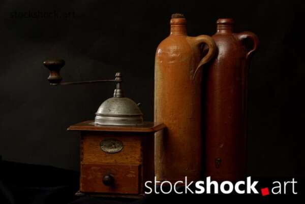 In this still life painting, we see a carefully composed scene in which a classic coffee grinder sits next to ceramic jugs.