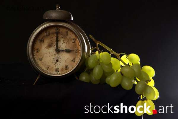 Clock, old alarm clock on black background with green grapes