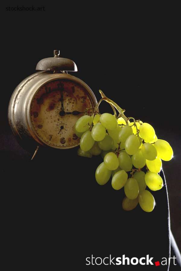 Clock, old alarm clock on black background with green grapes