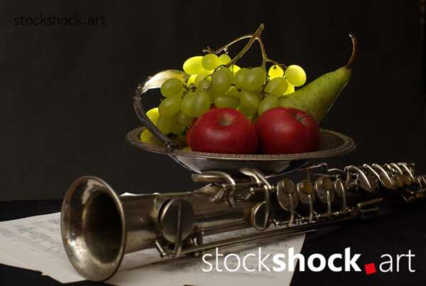 Still life on a black background with fruit on a platter and a clarinet