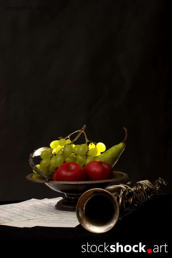 Still life on a black background with fruit on a platter and a clarinet