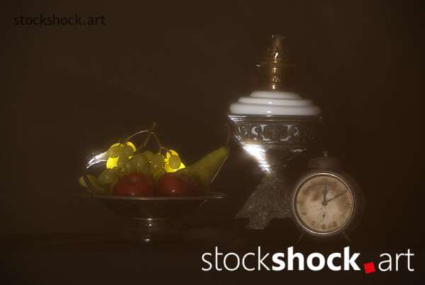 Still life composition consisting of elements such as an old oil lamp, fruits on a plate and a clock symbolizing the passing of time tick tock.