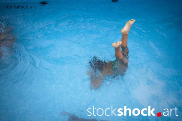 boy dives into the blue water of the pool, only his feet visible above the water